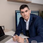 Businessman in blue suit working on laptop in sleek office setting, conveying professionalism and focus.