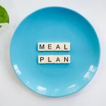 Innovative meal planning concept using alphabet tiles on a blue plate with green leaves.