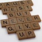 Wooden tiles spelling out 'Pause Rest But Never Give Up' on a white background.