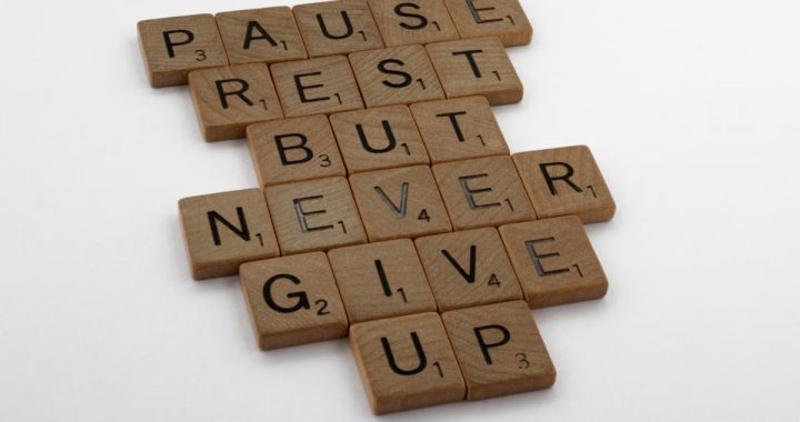 Wooden tiles spelling out 'Pause Rest But Never Give Up' on a white background.